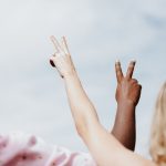 woman in white and pink floral shirt raising her hands